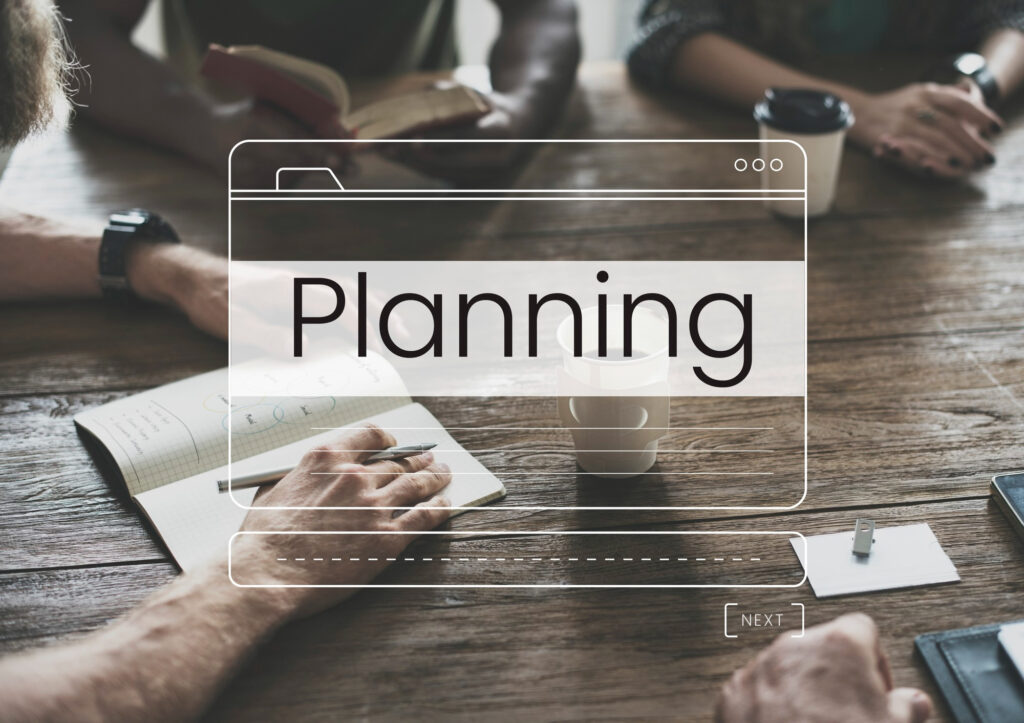 People are networking around a business table and their hands and notebooks are shown with an overlay of a folder with the word Planning
